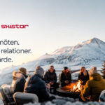 Deelnemers uit het bedrijfsleven verzamelden zich rond een kampvuur in een bergachtig gebied tijdens een fysiek evenement in een winters landschap. De afbeelding illustreert het groeiende belang van persoonlijke bijeenkomsten, conferenties en de bedrijfscultuur.